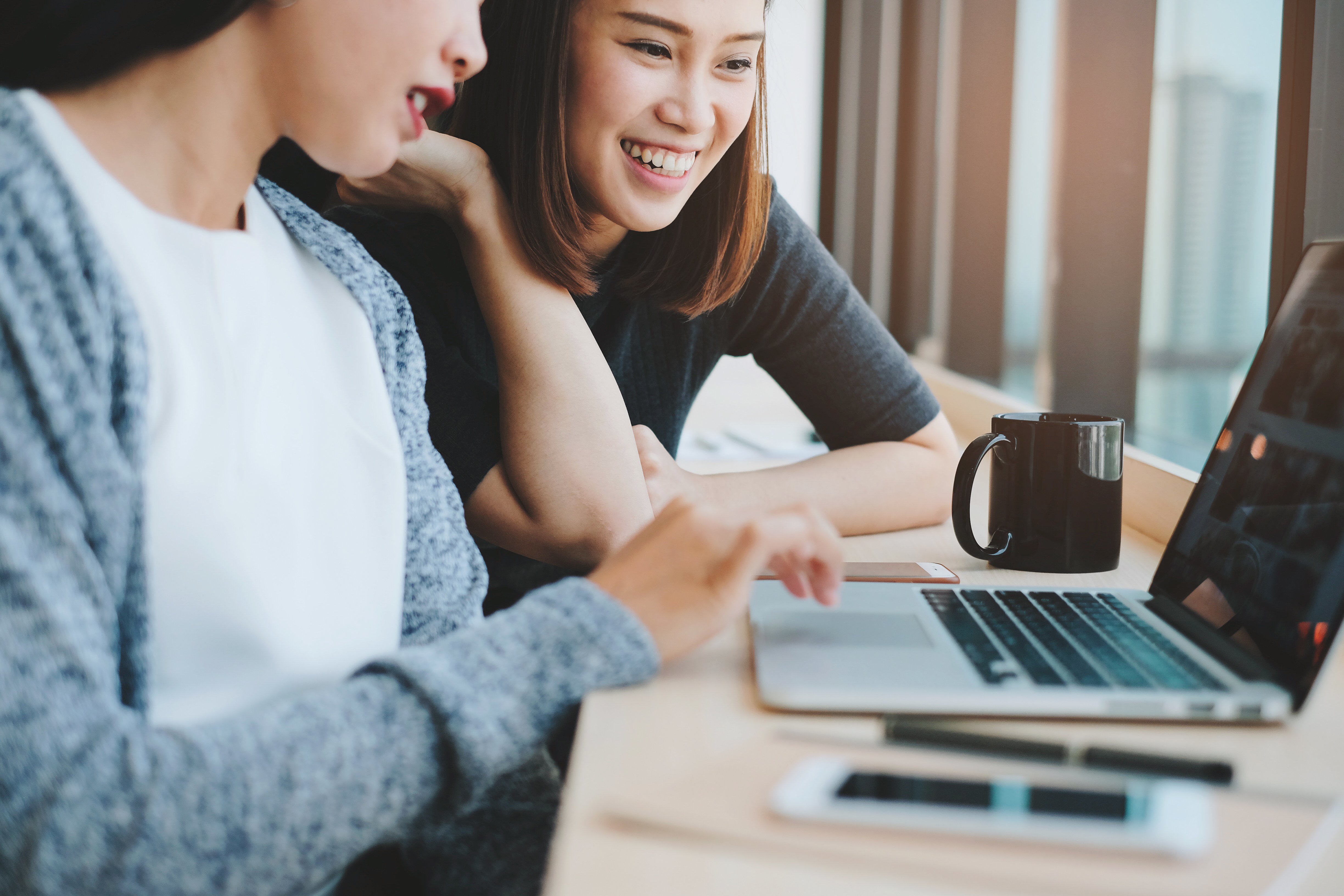 two-businesswomen-friends-smiling-and-brainstorming-while-using-laptop-in-office-or-cafe_t20_g8AZkG